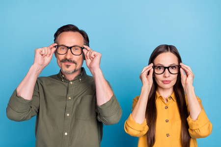 Photo of mature serious man and woman people wear glasses eyewear hold hands isolated on blue color...