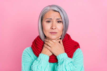 Photo of sad grey hairdo old lady ill wear scarf teal pullover isolated on pink color backgroundの写真素材