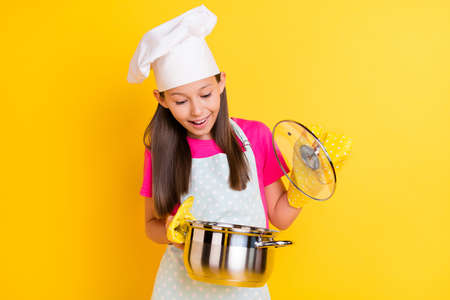 Photo of curious funny girl open saucepan look ingredients wear white apron hat isolated yellow color backgroundの写真素材