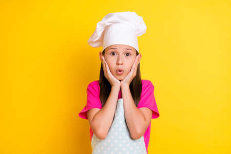 Photo of crazy speechless stunned girl hands cheeks open mouth wear white apron hat isolated yellow color backgroundの写真素材