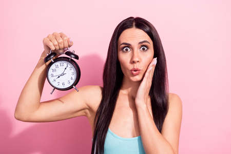 Photo of impressed pretty lady hold classic clock arm palm on cheek look camera isolated on pink color backgroundの写真素材