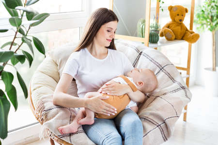 Portrait of attractive careful girl holding nursing baby spending day calm life at light home flat...