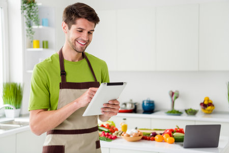 Portrait of attractive cheery guy preparing natural weight loss meal reading recipe ebook at light white kitchen home indoorsの写真素材