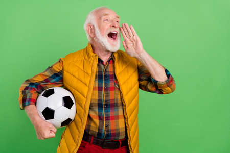 Photo of pretty funny mature man dressed yellow waistcoat holding ball making announcement empty space isolated green color backgroundの写真素材