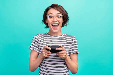Photo of lovely millennial brunette lady playstation wear eyewear striped t-shirt isolated on teal color backgroundの写真素材