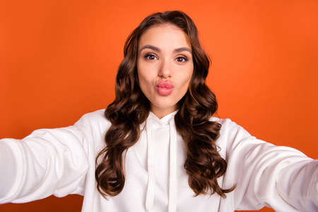 Photo portrait woman in casual outfit with long wavy hair sending air kiss taking selfie isolated vivid orange color backgroundの写真素材
