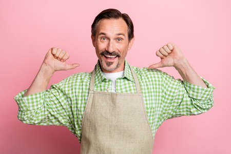 Photo of excited impressed young guy dressed beige apron plaid shirt smiling pointing fingers himself isolated light pastel pink color backgroundの写真素材