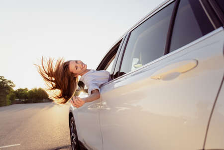 Photo of cute carefree young lady dressed white shirt smiling driving automobile looking window outdoors urban routeの写真素材