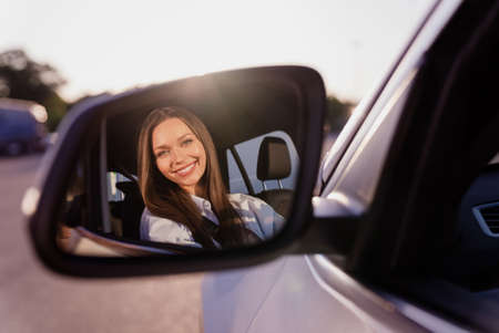 Photo of sweet cute young lady dressed white shirt smiling looking back mirror driving automobile...