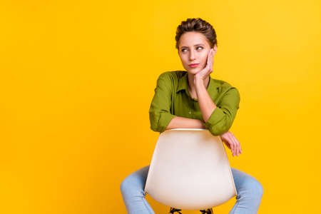 Photo of minded lady sit chair hand cheek look empty space wear green shirt isolated yellow color backgroundの写真素材