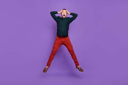Photo of excited shocked young guy dressed smart casual clothes jumping high arms head isolated violet color backgroundの写真素材