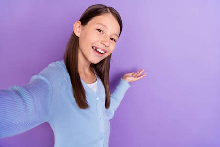 Photo of sweet brunette little girl do selfie hold empty space wear blue shirt isolated on violet...