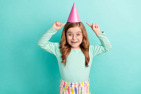 Photo of young little girl happy positive smile point fingers cap celebration holiday isolated over teal color backgroundの写真素材