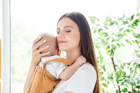 Photo of adorable sweet mother dressed white t-shirt holding hands arm child smiling inside indoors...