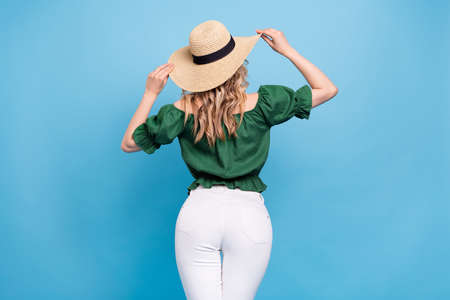 Rear back view photo of tourist lady wear straw hat bear shoulders green blouse pants isolated blue color backgroundの写真素材