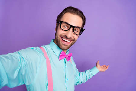 Photo of young brunet funky guy hold empty space wear tie suspenders blue shirt eyewear isolated on...