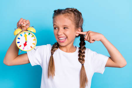 Photo of young little girl close finger ears loud noise clock timer alarm isolated over blue color backgroundの写真素材