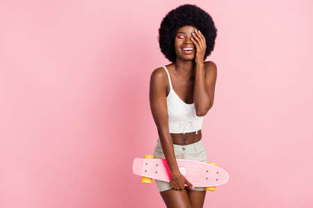 Photo of lovely young curly hairdo lady hold skate closed eyes wear white top shorts isolated on pastel pink color backgroundの写真素材