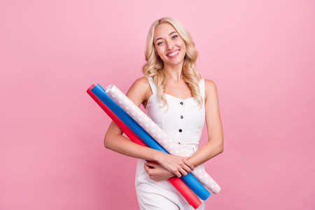 Photo of charming pretty young lady wear white overall smiling holding wrapping paper rolls isolated pink color backgroundの写真素材