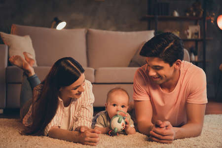 Portrait of full tender adorable attractive cheerful family parenthood lying on carpet playing with baby enjoying at home indoorsの写真素材