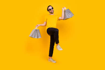 Full length photo of young excited man good mood hold shopping bag store go walk isolated over yellow color backgroundの写真素材