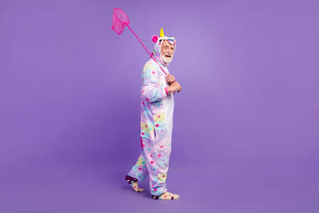 Photo of charming funny man pensioner unicorn sleepwear walking catching butterflies smiling...