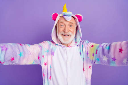 Self-portrait of attractive cheerful grey-haired man wearing kigurumi good mood isolated on violet purple color backgroundの写真素材
