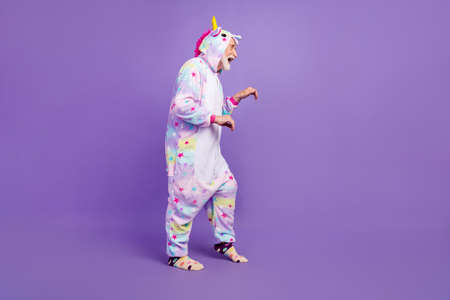 Photo of handsome funny man pensioner unicorn sleepwear dark stealing toes smiling isolated violet...