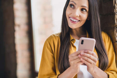 Photo of charming thoughtful young lady dressed yellow shirt writing modern device smiling indoors...
