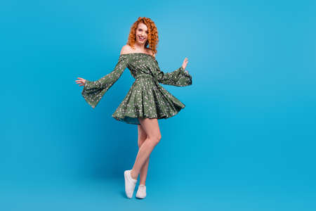 Full length photo of optimistic lady dance wear green dress sneakers isolated on blue color backgroundの写真素材