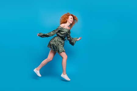 Full body profile photo of active orange hairdo lady run wear dress sneakers isolated on blue backgroundの写真素材