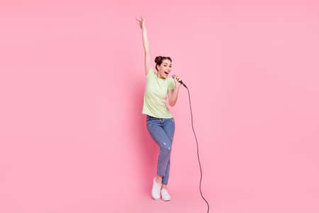 Photo of nice crazy lady hold microphone sing raise hand wear green t-shirt jeans footwear isolated...
