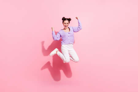 Full length body size photo of cheerful girl jumping high careless gesturing like winner isolated on pastel pink color backgroundの写真素材