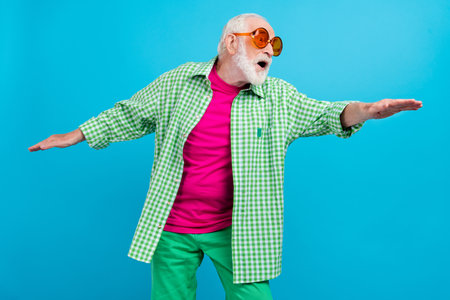 Photo of amazed happy cheerful old man look empty space good mood hands wings isolated on blue color...
