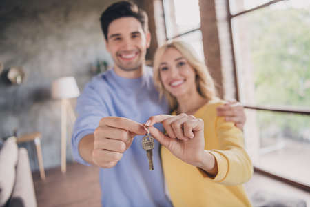 Portrait of handsome beautiful trendy cheerful couple holding key new flat buy at home loft industrial interior indoorsの写真素材