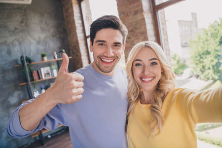 Self-portrait of handsome beautiful cheerful couple showing thumbup positive at home loft industrial interior indoorsの写真素材