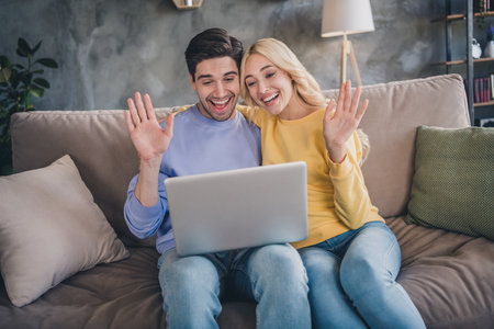 Portrait of handsome beautiful trendy cheerful couple sitting on divan making video call at home loft industrial interior indoorsの写真素材