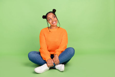 Full length photo of cozy shape young brunette lady sit look empty space wear pullover jeans footwear isolated on green backgroundの写真素材