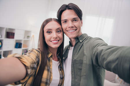Photo of charming sweet young couple wear casual outfits smiling embracing recording self video indoors house roomの写真素材