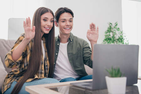 Photo of charming beautiful young lovers dressed casual clothes sitting sofa talking modern device waving arms smiling indoors apartmentの写真素材