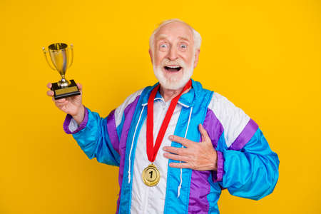 Photo of excited grandfather win prize omg wow first place competition practice isolated over yellow color backgroundの写真素材