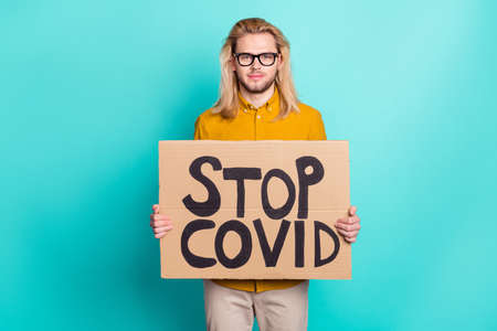 Photo of young guy hold banner stop covid coronavirus protest strike lockdown isolated over teal color backgroundの写真素材