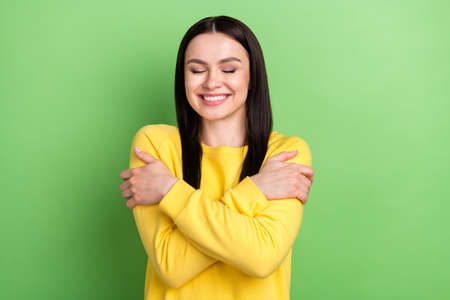 Portrait of attractive dreamy glad cheerful girl hugging herself good mood isolated over bright green color backgroundの写真素材