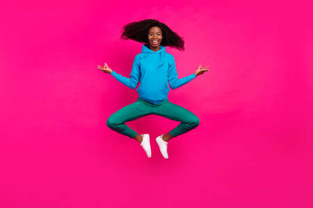 Photo of funny peaceful dark skin woman dressed blue sweatshirt smiling jumping high practicing yoga isolated pink color backgroundの写真素材