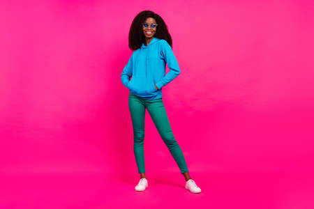 Photo of confident charming dark skin lady wear blue hoodie glasses arms pockets smiling isolated...