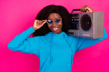 Photo of cool sweet dark skin woman dressed blue sweatshirt arm eyewear smiling listening boombox isolated pink color backgroundの写真素材