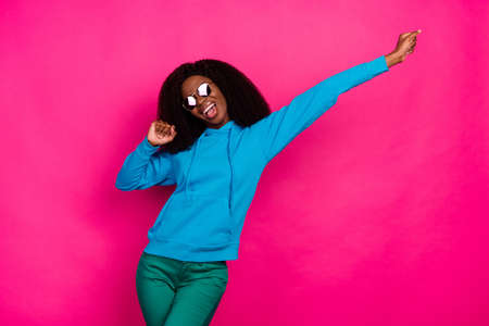 Photo of cute funky dark skin woman dressed blue sweatshirt eyewear smiling dancing isolated pink...