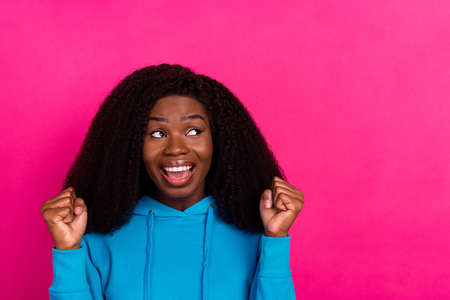 Photo of charming happy dark skin woman look empty space raise fists winner isolated on pink color backgroundの写真素材