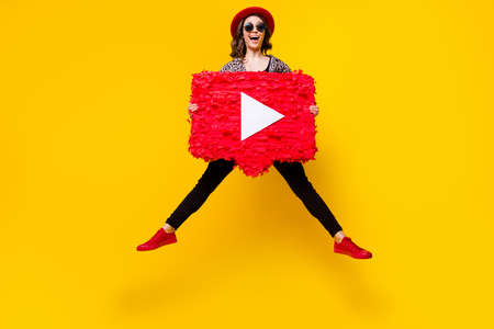 Full body photo of cheerful happy young woman hold hand icon play video jump up isolated on yellow color backgroundの写真素材