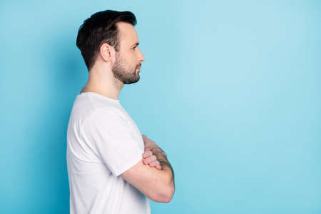 Profile photo of young person folded arms look attentively empty space isolated on blue color...